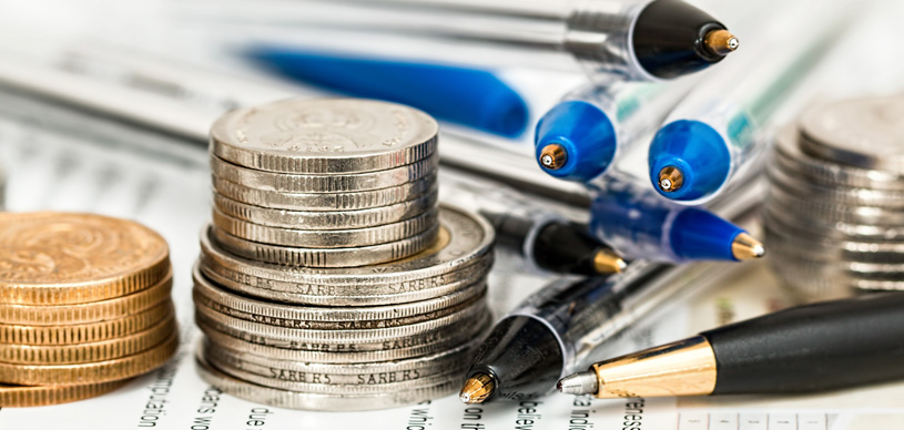 Na imagem mostra algumas moedas e canetas para representar o orçamento ajustado. 